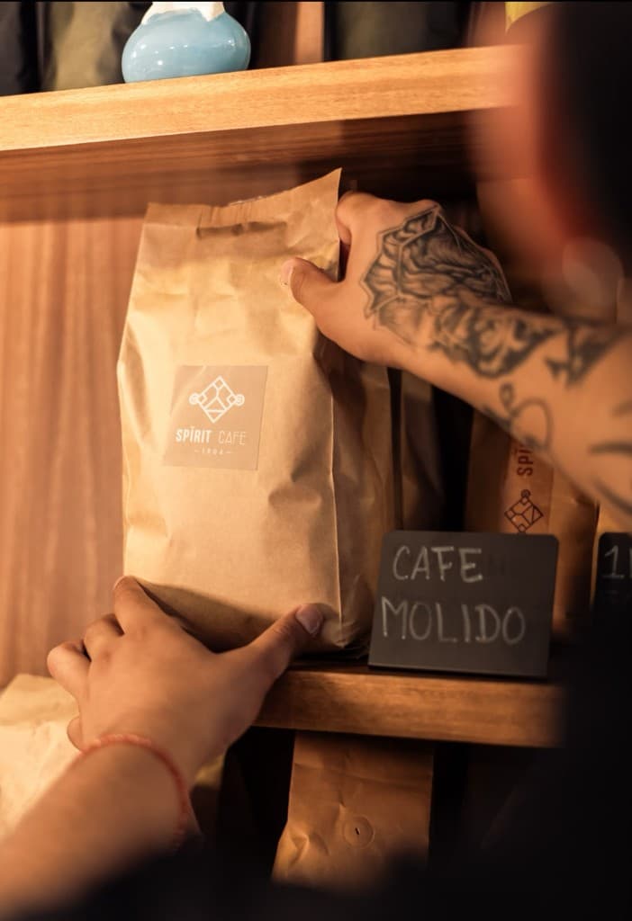 Hands lifting a Spirit Café ground coffee bag from the shelf.